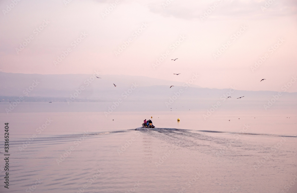 Fototapeta premium Fishermen leave to collect catches from pots. Sunrise over lake Geneva as the crew and their small boat head out from shore to check their morning catch.