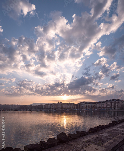 Stunning morning sunrise over the harbor and residential district of Geneva, Switzerland. The clouds and sun rays break over the building roofs in this early morning shot.