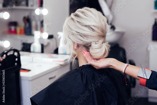 hair stylist makes her hair into a bun on the head of a blonde girl with long hair