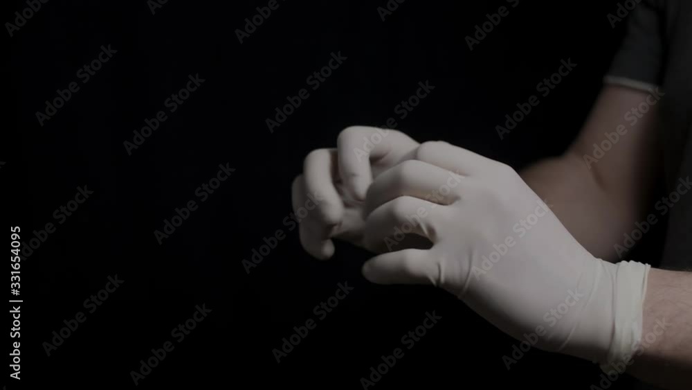 The doctor puts on protective white gloves on a black background The doctor puts on protective white gloves on a black background