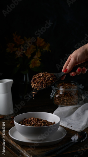 Chocolate granola in white bowl. Dark key photo style. cozy home  homemade breakfast