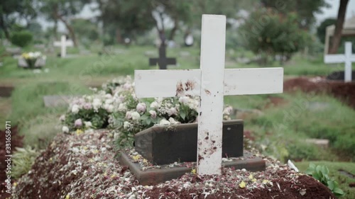 Christian grave with white cross and flower bouquets at cemetery seen from behind photo