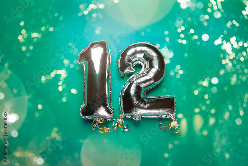 Silver Number Balloons 12 on green background with bokeh lights. Holiday Party Decoration or postcard concept with top view