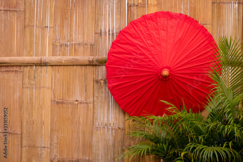 Red paper umbrella with green palm leaves on bamboo wooden wall background   wall decoration design concept