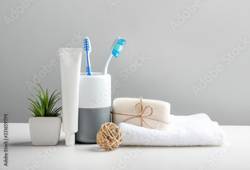 Toothbrushes in cup  toothpaste and bath towels on grey background