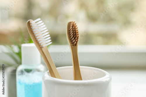 Wooden toothbrushes in cup and mouthwash in bathroom near window