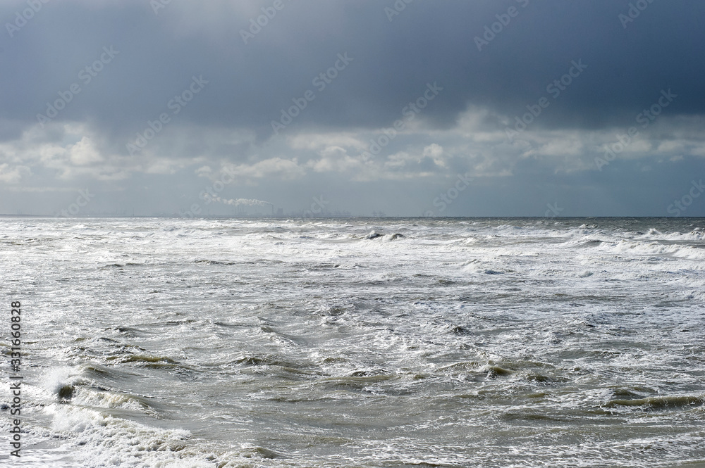 The Hague, South-Holland/Netherlands - 200226: Wild sea with waves on a stormy day. Industrial area at the horizon