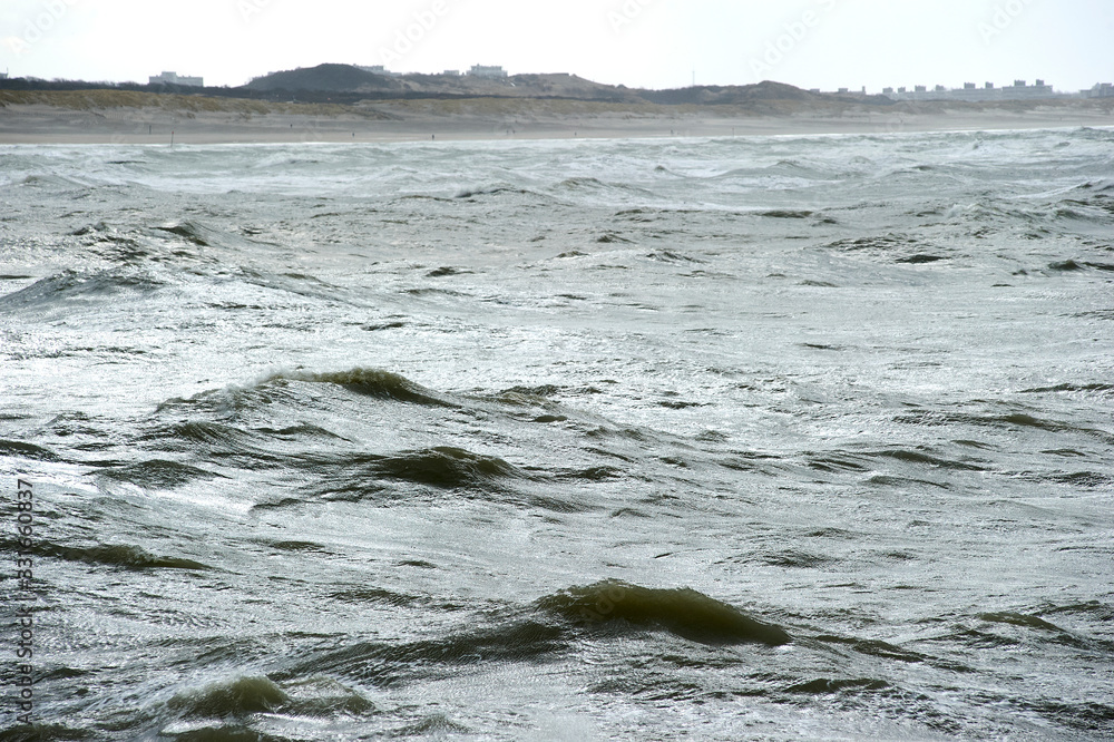 Fototapeta premium The Hague, South-Holland/Netherlands - 200226: Wild sea with waves on a stormy day with dunes and houses on the background