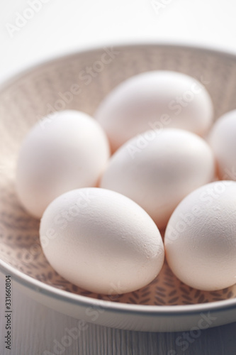 Eggs with white shells in a ceramic bowl on a white wooden table close up view