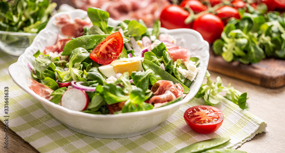 Fresh spring salad with green leaves tomatoes egg radish red onion young peas prosciutto feta cheese and olive oil