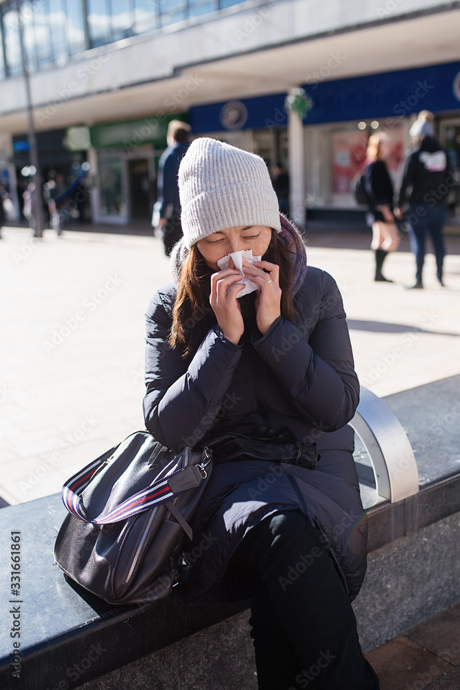 Fototapeta premium Nice Asian young woman wiping her nose in the sreet