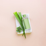 Aloe vera natural cosmetic product bottle with gel, toner or lotion with green mock up for branding and fresh aloe vera leaves on white towel on pastel background. Top view. Modern skin care. Beauty
