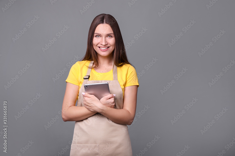 Young woman in an apron with tablet on gray background. Young woman in an apron with tablet on gray background.