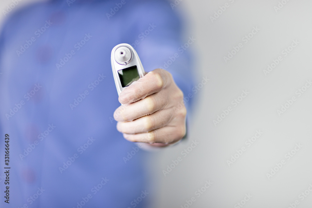 Fototapeta premium Lekarz w niebieskiej koszuli na jasnym tle trzymający w dłoni termometr