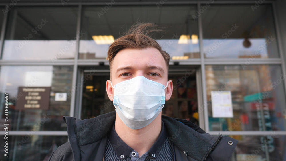 Portrait of young man with medical face mask stands outdoor. Time lapse of guy wearing protective mask from virus outside. Concept of health and safety life from coronavirus and pandemic. Timelapse