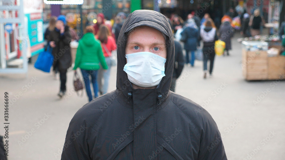 Portrait of young man with medical face mask stands at city street. Guy wearing protective mask from virus outdoor in the people crowdy. Concept of health and safety life from coronavirus and pandemic Portrait of young man with medical face mask stands at city street. Guy wearing protective mask from virus outdoor in the people crowdy. Concept of health and safety life from coronavirus and pandemic