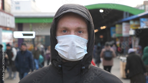 Portrait of young man with medical face mask stands at city street. Guy wearing protective mask from virus outdoor in the people crowdy. Concept of health and safety life from coronavirus pandemic