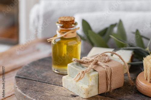 Concept of natural ingredients in cosmetology for gentle skin care. Organic olive oil in glass bottle, handmade soap bars. Atmosphere of serenity and relax. Rustic wooden background, close up.