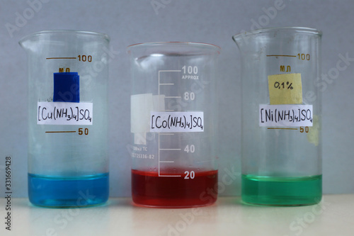 Reagents for the preparation of ammonia complexes compounds: blue copper sulfate, red cobalt sulfate, green nickel sulfate, aqueous solutions in beakers.