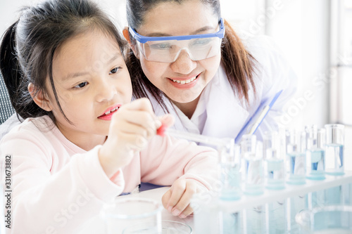 Asian girl school student performing experiment in chemistry lab with scientist teacher