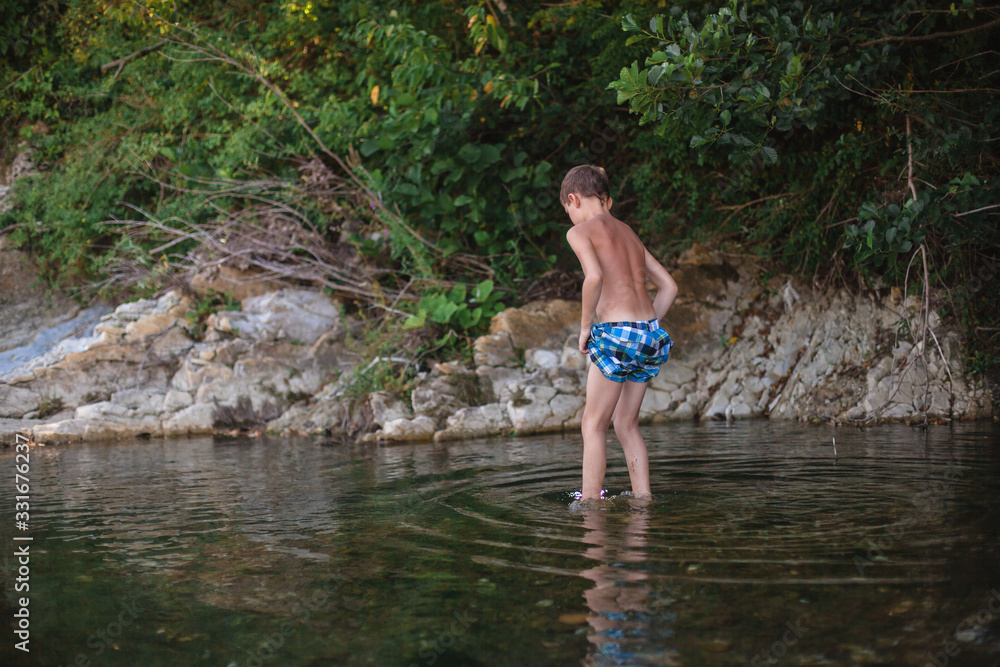 A teenage boy in shorts plays in a mountain river in shallow water A teenage boy in shorts plays in a mountain river in shallow water