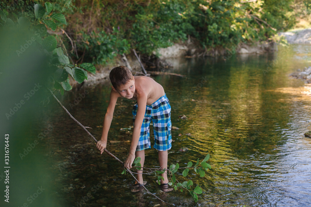 A teenage boy in shorts plays in a mountain river in shallow water A teenage boy in shorts plays in a mountain river in shallow water