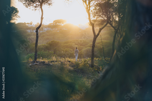 Young woman in distance enjoying the walk in the forest at sunset