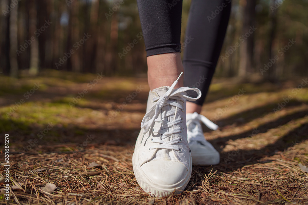 Walking on a path in a pine forest.  White women's sneakers. 