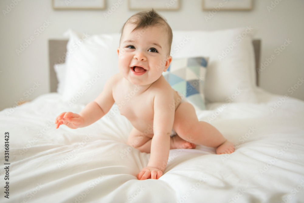Cute baby girl sitting on the white bedding and smiling Cute baby girl sitting on the white bedding and smiling