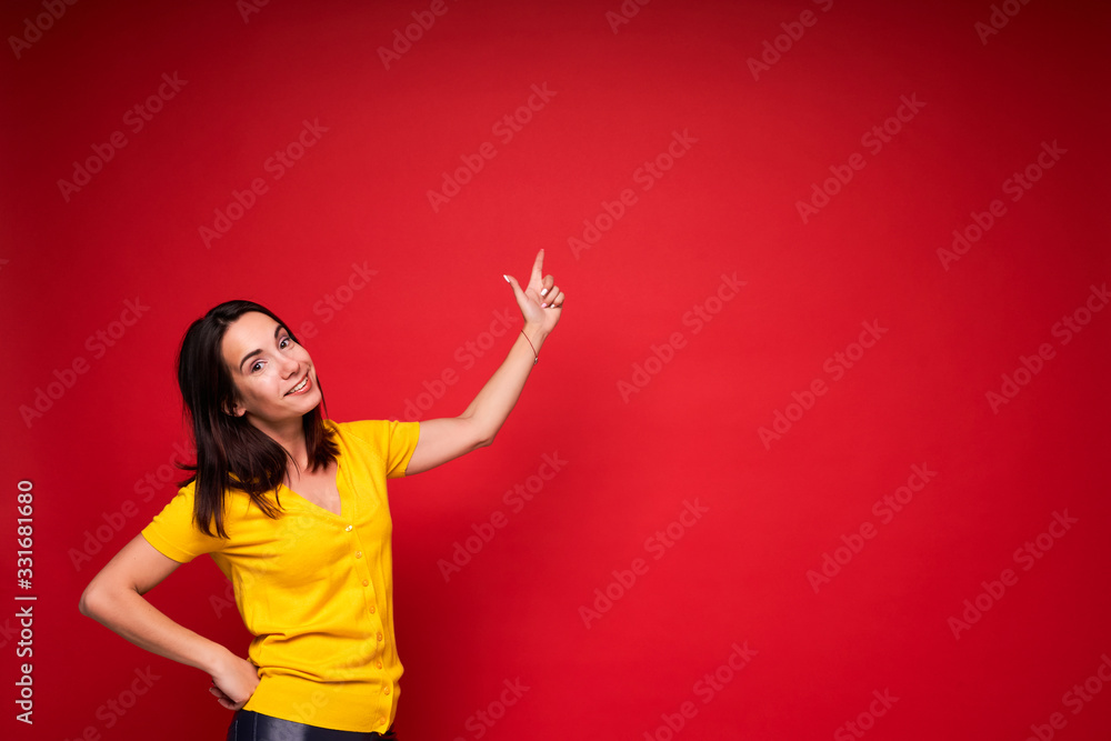Happy successful young woman with raised arm pointing her finger to the side on red background Happy successful young woman with raised arm pointing her finger to the side on red background