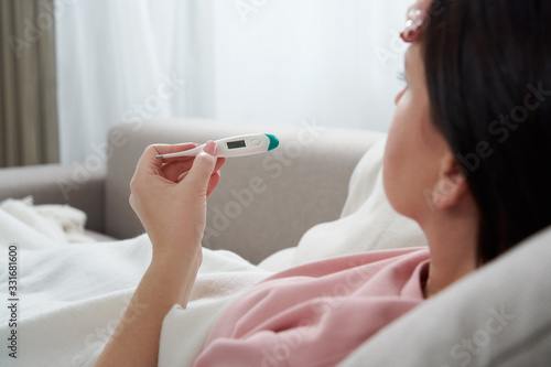 Woman looking at thermometer. Female hands holding a digital thermometer. Concept of fever, flue or virus photo