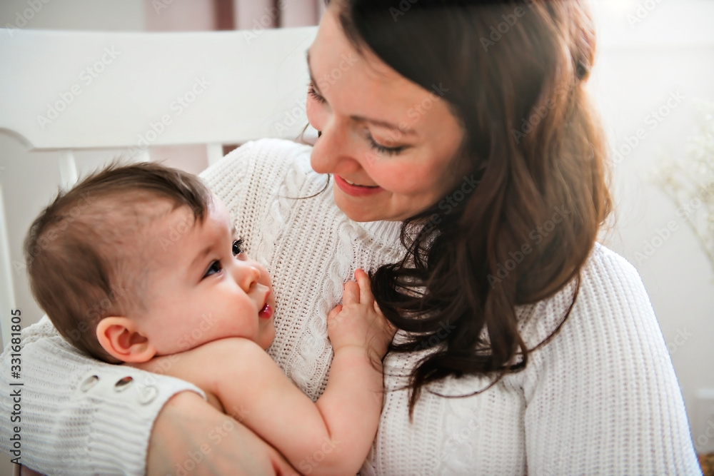 A young mother with a baby in a beautiful bedroom with window on the back A young mother with a baby in a beautiful bedroom with window on the back