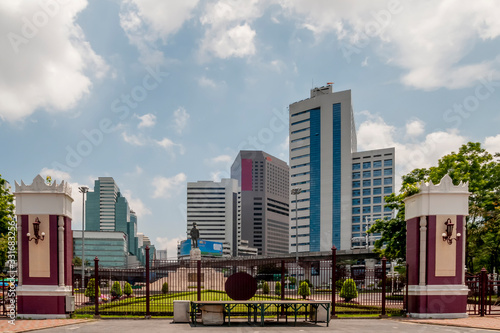 One of the entrances to Lumphini Park in Bangkok, Thailand, with the monument to King Rama VI and the skyscrapers of Silom in the background