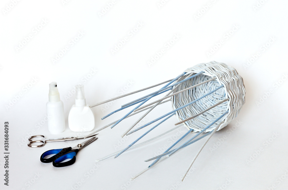 Hobbies and leisure. Weaving a basket of paper tubes for a gift. Interesting craft in your free time. White background, free space for text Hobbies and leisure. Weaving a basket of paper tubes for a gift. Interesting craft in your free time. White background, free space for text