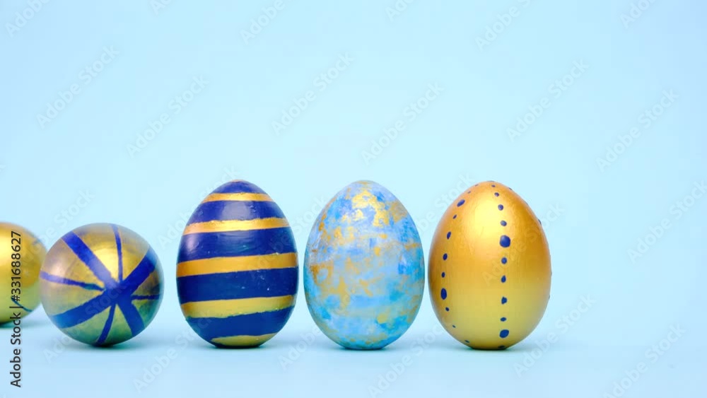 Easter eggs are rolling, knocking each other on blue table. Eggs trendy colored classic blue, white and golden . Happy Easter. Minimal style Easter eggs are rolling, knocking each other on blue table. Eggs trendy colored classic blue, white and golden . Happy Easter. Minimal style