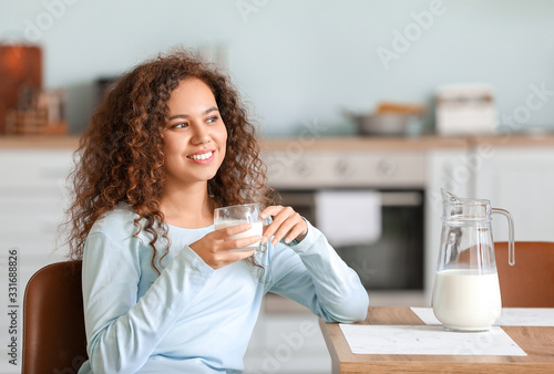Foto Young African-American woman with milk in kitchen