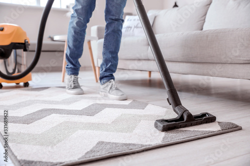 Young man hoovering floor at home