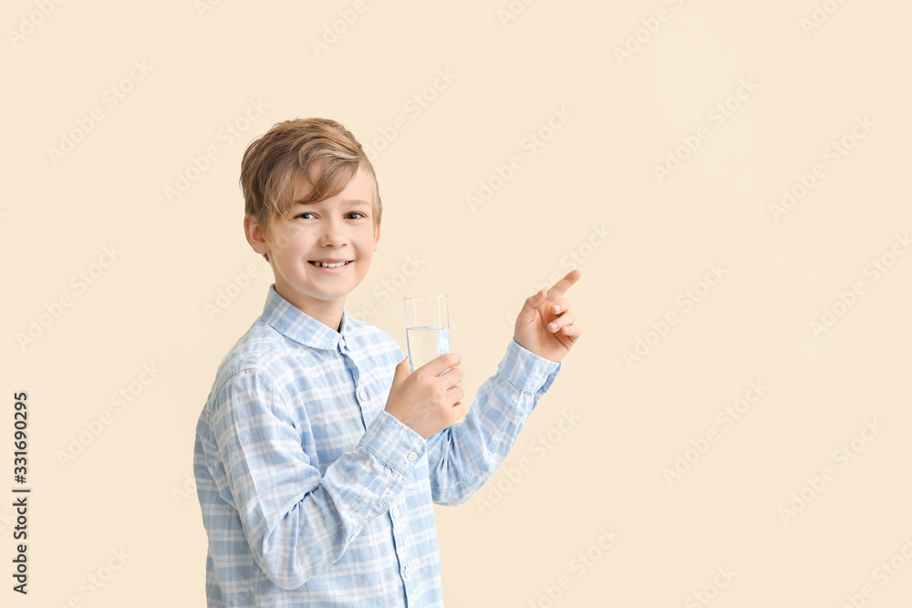 Cute little boy with glass of water pointing at something on color background Cute little boy with glass of water pointing at something on color background