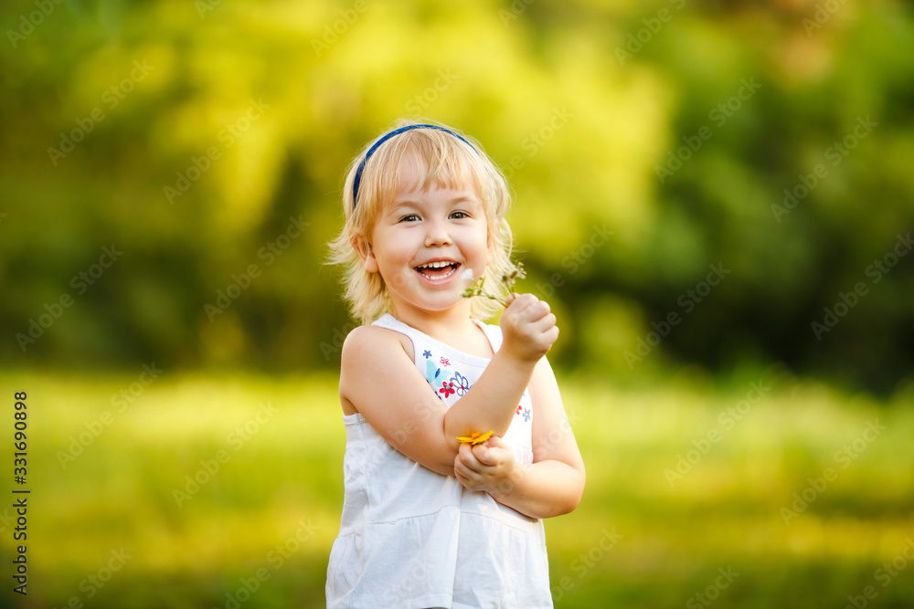 Little blonde 2-3 years old girl playing in the summer park and smelling flowers. Children activity concept
