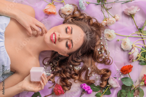 Portrait of beautiful young woman with bottle of perfume and flowers