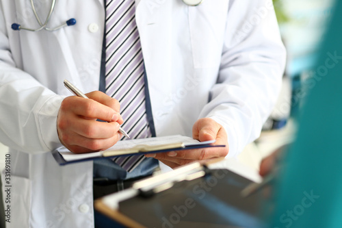 Doctor making simple notes in notepad. Smart doc wearing white robe and trendy tie with stripes. Professional physician posing in clinic. Medical treatment concept