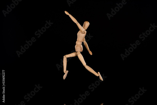 Wooden puppet imitating jumping on black background