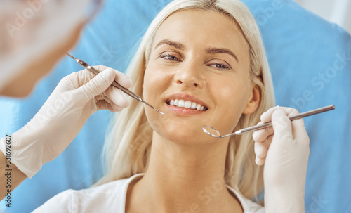 Smiling blonde woman examined by dentist at dental clinic. Healthy teeth and medicine concept