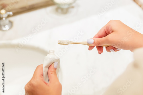 Cropped image of female hands putting toothpaste on the toothbrush in the bathroom. Dental care concept. Preparation for teeth cleaning
