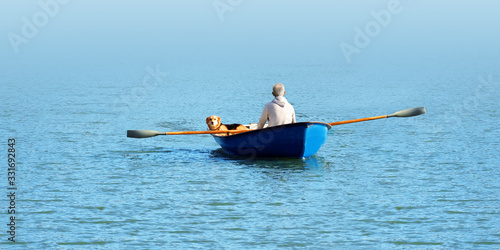 Elderly man and a dog swim in a boat in the water, panoramic view © ANGHI
