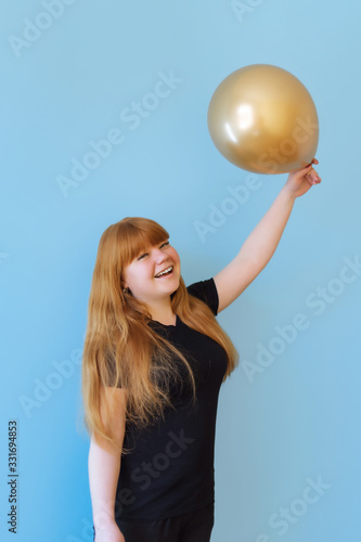 birthday, valentines day concept. Happy red-haired girl holding a bouquet of gold-colored balloons on a blue background, the girl is happy