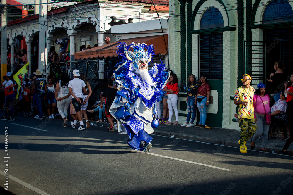 tall person in variegated costume pass by city street at dominican carnival