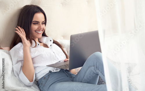 Girl waving hand on Video call. Girl working from home on laptop laying in bed