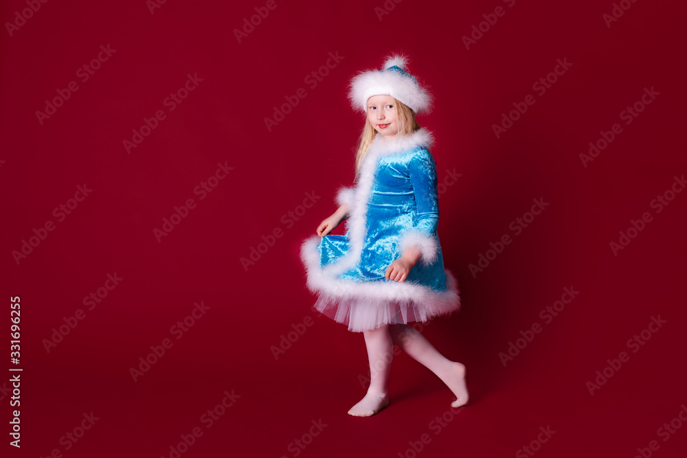Little blonde girl in a christmas and new year Santa costume having fun and sending kisses on red background. Space for text. Dreams come true Merry Christmas Little blonde girl in a christmas and new year Santa costume having fun and sending kisses on red background. Space for text. Dreams come true Merry Christmas