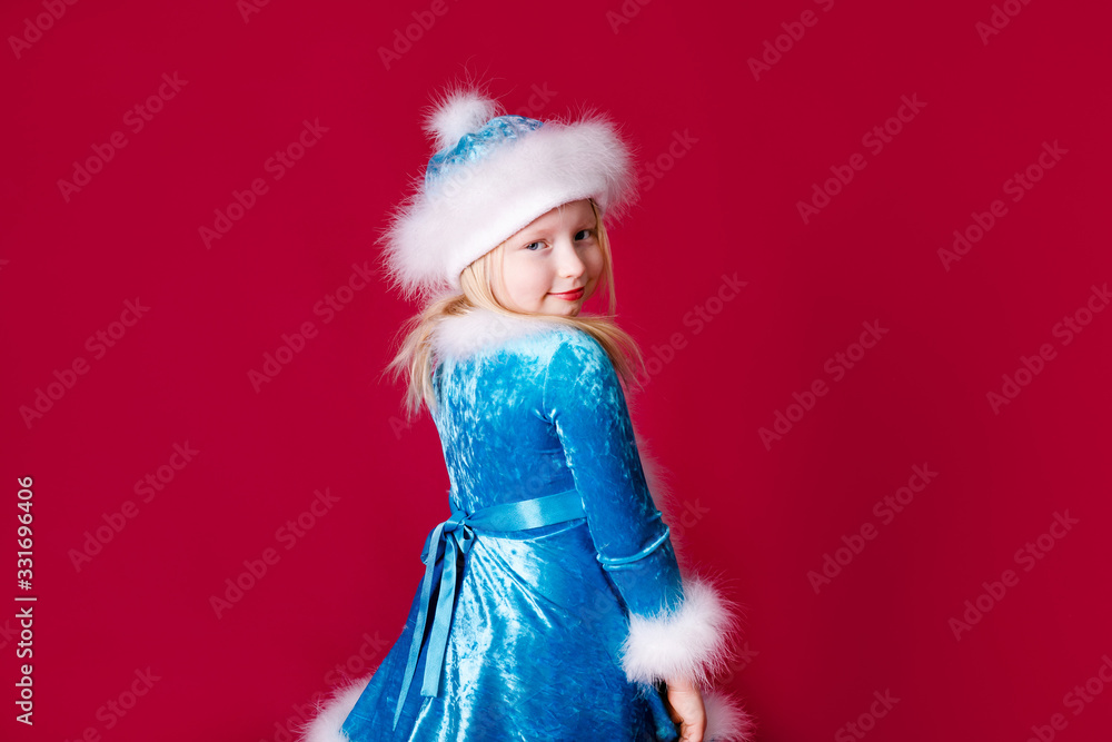 Little blonde girl in a christmas and new year Santa costume having fun and sending kisses on red background. Space for text. Dreams come true Merry Christmas